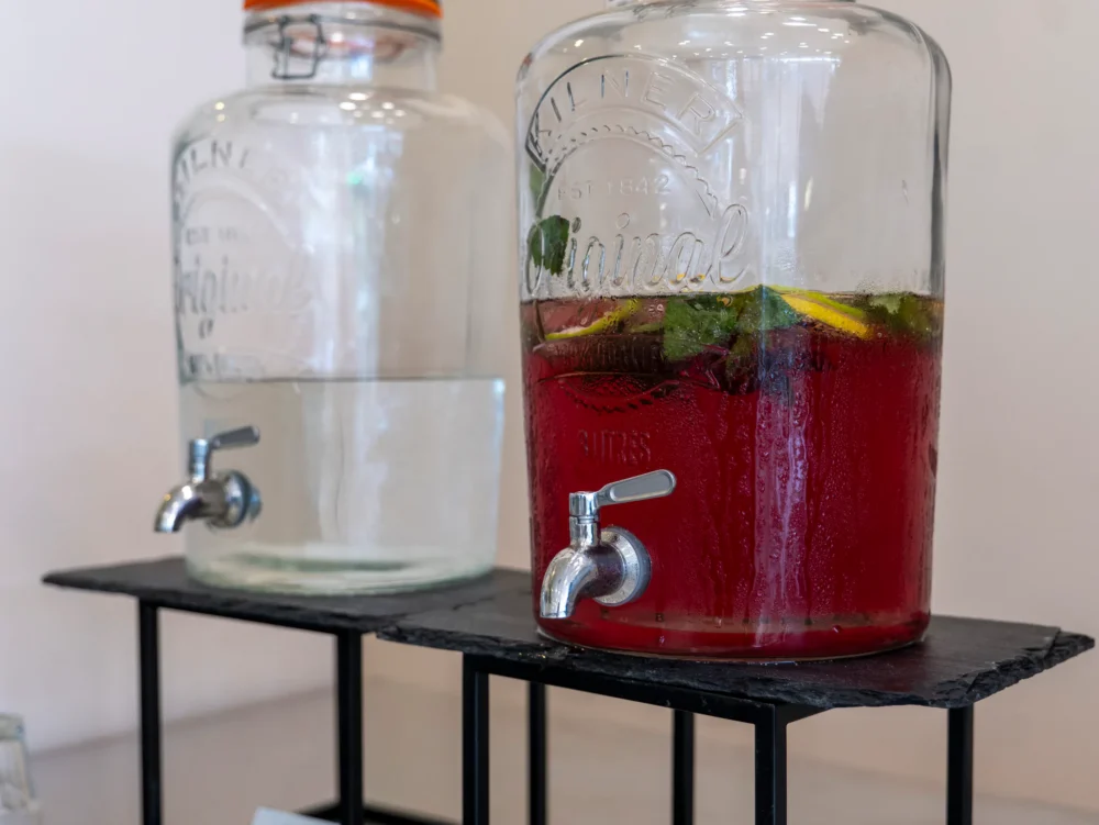 Dva skleněné barely s kohoutkem – čistá voda a domácí ovocná limonáda s mátou a citronem
