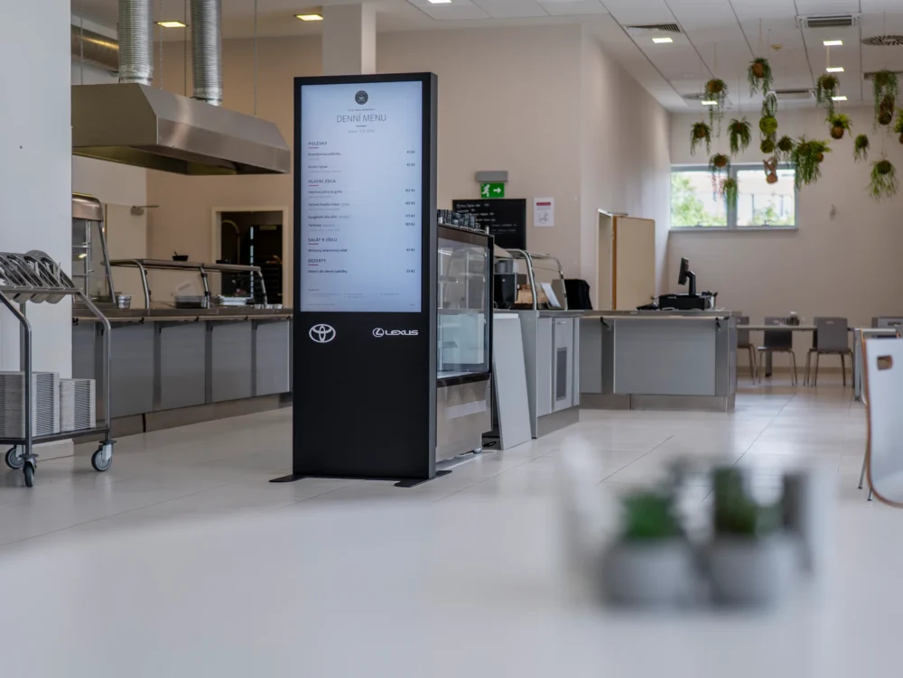 Stojan s denním menu u výdejní linky, nad ní závěsné rostliny